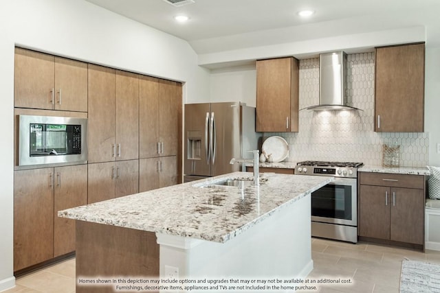 kitchen with decorative backsplash, stainless steel appliances, a kitchen island with sink, and wall chimney range hood