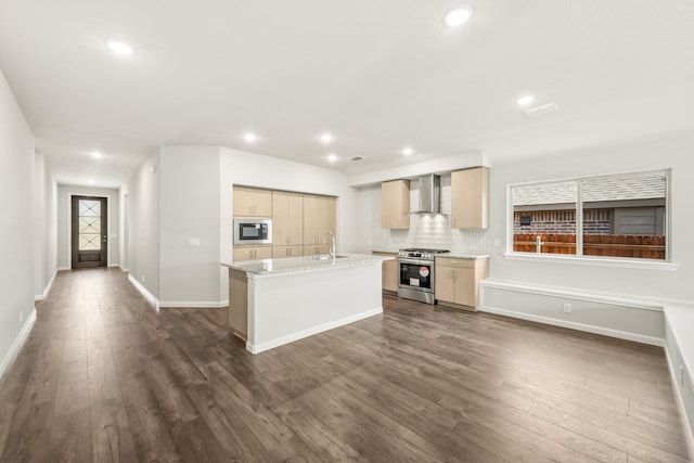 kitchen with an island with sink, backsplash, dark wood-type flooring, wall chimney exhaust hood, and appliances with stainless steel finishes