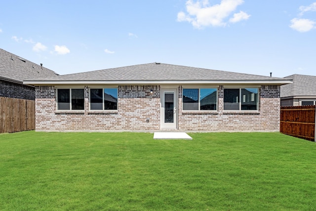 back of house with brick siding, a shingled roof, a yard, and fence private yard