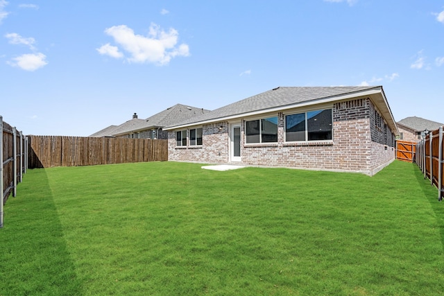 back of house with a shingled roof, a yard, a fenced backyard, and brick siding