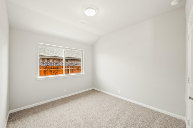 spare room with carpet flooring, visible vents, baseboards, and vaulted ceiling