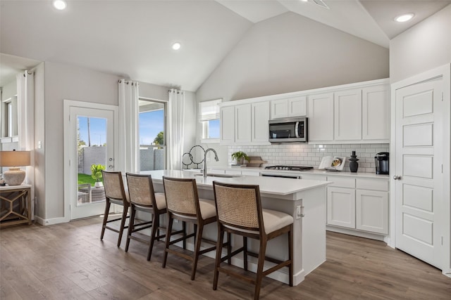 kitchen featuring white cabinetry, wood-type flooring, sink, a breakfast bar area, and an island with sink