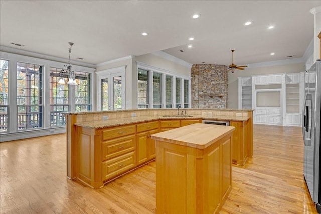 kitchen with light wood-type flooring, stainless steel refrigerator, a kitchen island, hanging light fixtures, and butcher block counters