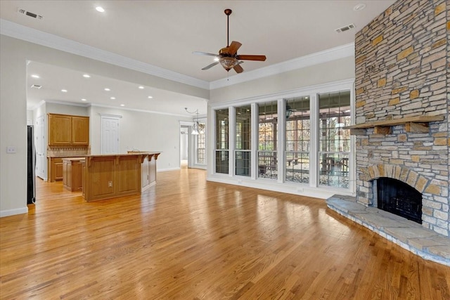 unfurnished living room with ceiling fan with notable chandelier, ornamental molding, a fireplace, and light hardwood / wood-style flooring