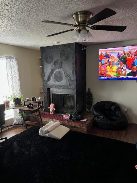 living room with wood-type flooring, a brick fireplace, and a textured ceiling