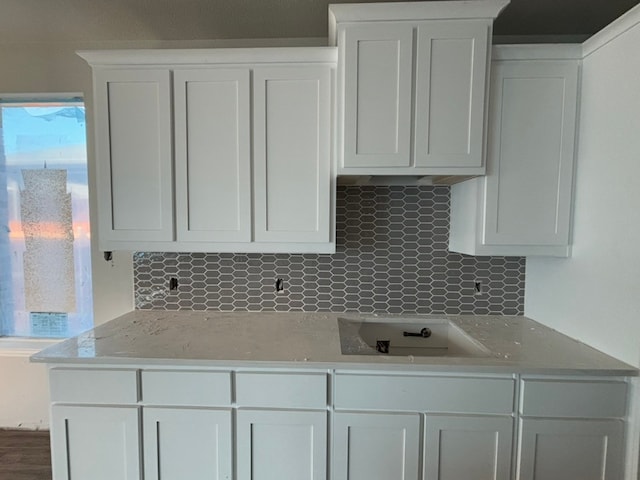 kitchen with light stone counters, backsplash, white cabinetry, and cooktop