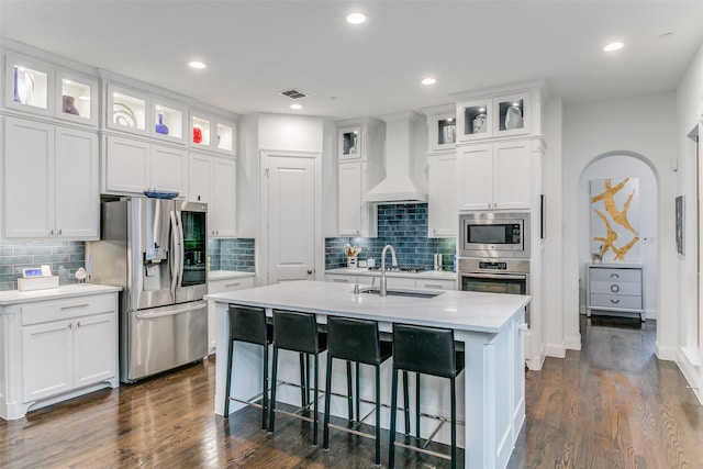 kitchen with a center island with sink, white cabinets, custom range hood, and appliances with stainless steel finishes