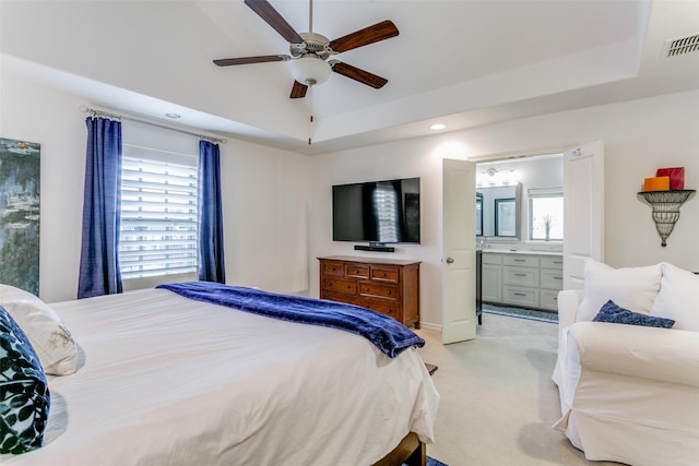 bedroom featuring light carpet, a tray ceiling, ensuite bath, and ceiling fan