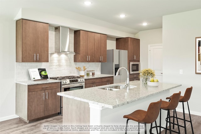 kitchen featuring a breakfast bar, sink, a center island with sink, stainless steel appliances, and wall chimney range hood