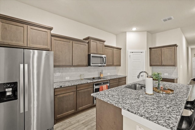 kitchen featuring decorative backsplash, stainless steel appliances, sink, a center island with sink, and dark stone countertops