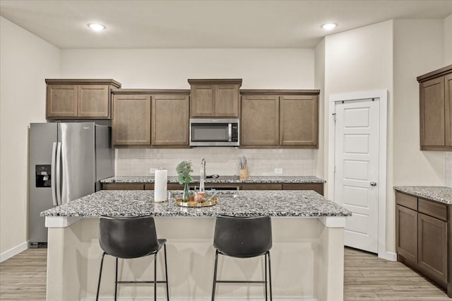 kitchen featuring light stone countertops, stainless steel appliances, tasteful backsplash, a center island with sink, and light wood-type flooring