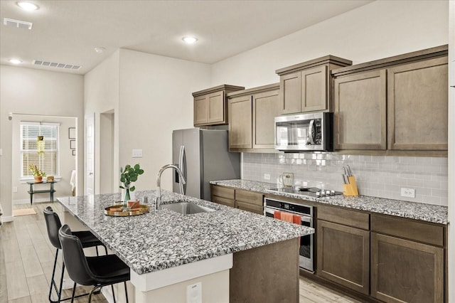 kitchen with a center island with sink, sink, light hardwood / wood-style flooring, light stone countertops, and appliances with stainless steel finishes