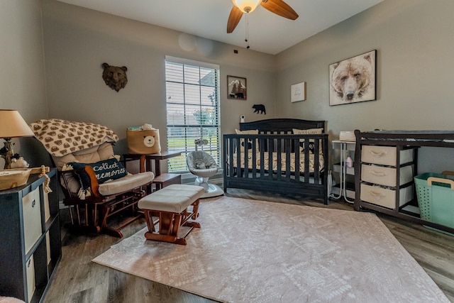 bedroom featuring ceiling fan, hardwood / wood-style floors, and a crib