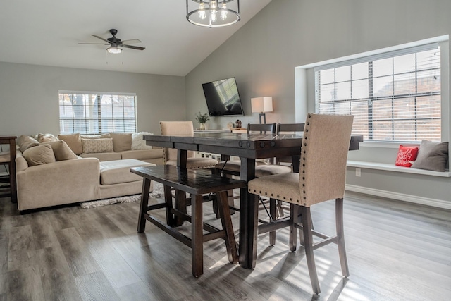 dining room featuring high vaulted ceiling, ceiling fan with notable chandelier, and wood-type flooring