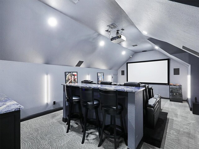 home theater room featuring lofted ceiling, light colored carpet, and a textured ceiling