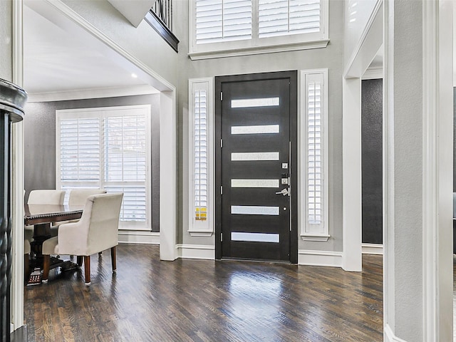 foyer with dark wood-type flooring, ornamental molding, and a high ceiling