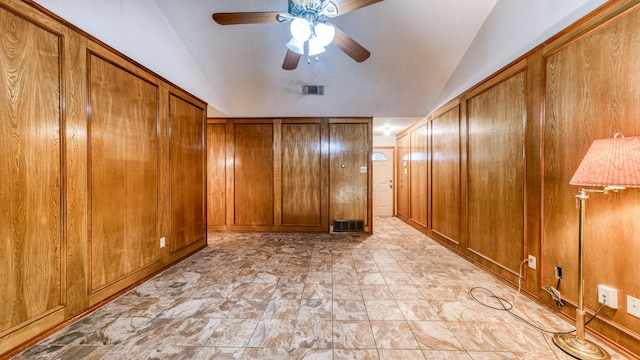 empty room with ceiling fan, wood walls, lofted ceiling, and a textured ceiling