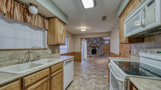 kitchen featuring a textured ceiling, a stone fireplace, sink, and white appliances