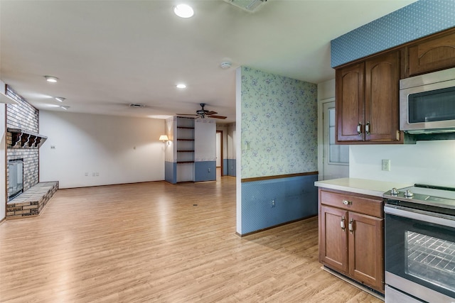 kitchen with ceiling fan, light wood-type flooring, a fireplace, and appliances with stainless steel finishes