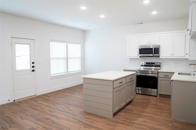 kitchen with appliances with stainless steel finishes, gray cabinetry, tasteful backsplash, dark wood-type flooring, and sink