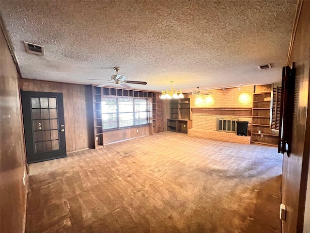 unfurnished living room with a textured ceiling, ceiling fan with notable chandelier, wooden walls, a fireplace, and carpet floors