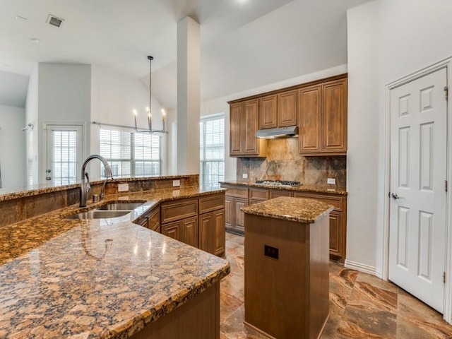 kitchen featuring stainless steel gas cooktop, sink, a center island, stone counters, and pendant lighting