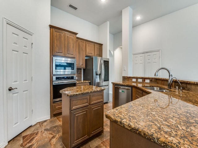 kitchen with sink, stone counters, backsplash, stainless steel appliances, and a center island