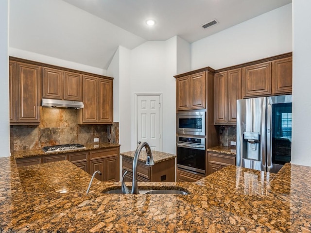 kitchen featuring lofted ceiling, sink, tasteful backsplash, dark stone counters, and stainless steel appliances