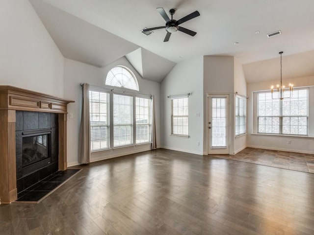 unfurnished living room featuring lofted ceiling, dark hardwood / wood-style floors, a tiled fireplace, and ceiling fan with notable chandelier