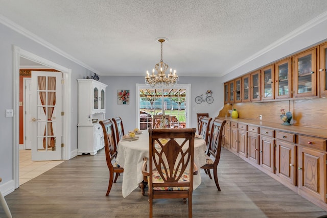 dining area with an inviting chandelier, light hardwood / wood-style flooring, ornamental molding, and a textured ceiling