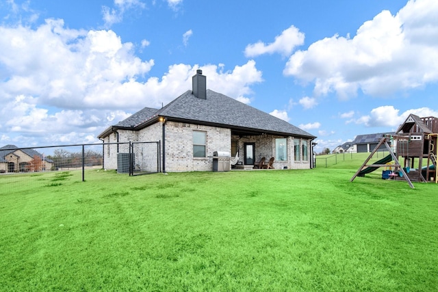 back of house featuring brick siding, a shingled roof, a playground, a chimney, and a yard