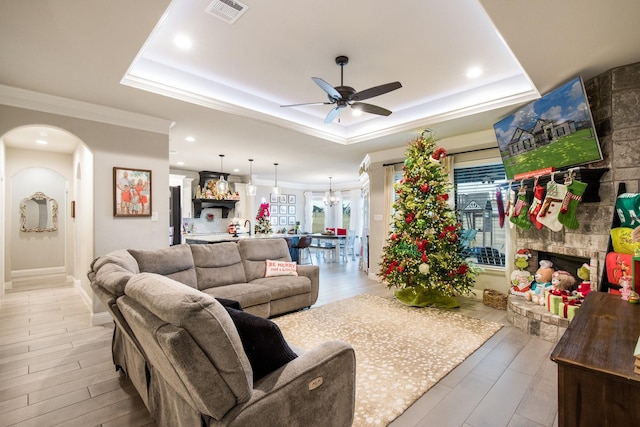 living room with ceiling fan with notable chandelier, light wood-type flooring, a raised ceiling, and crown molding