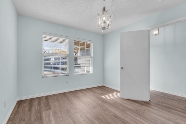 empty room with a textured ceiling, light hardwood / wood-style floors, and an inviting chandelier