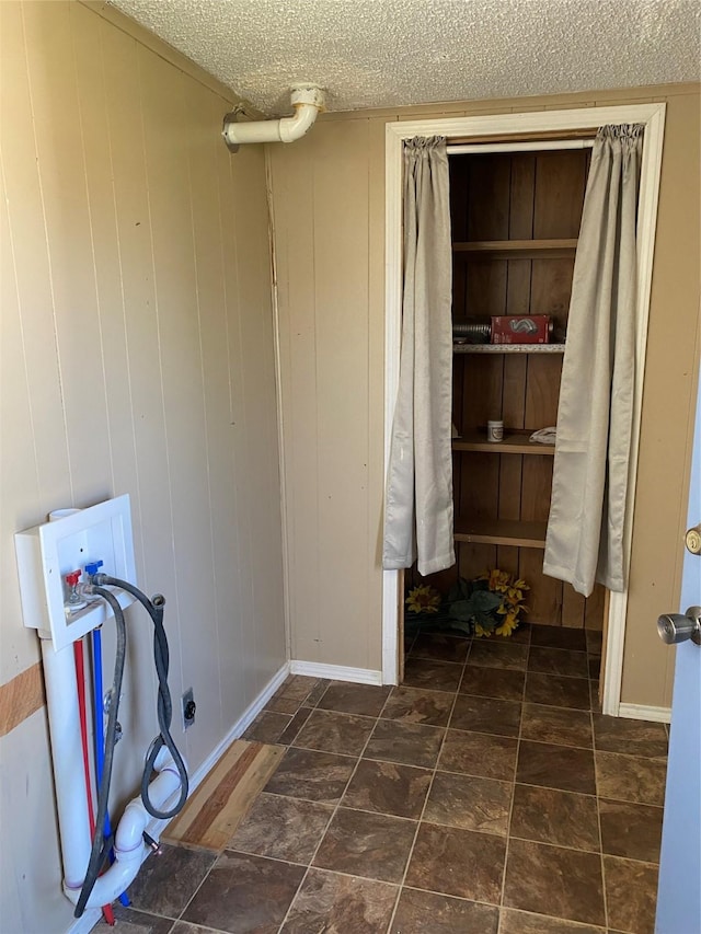 clothes washing area with wood walls, a textured ceiling, and hookup for a washing machine