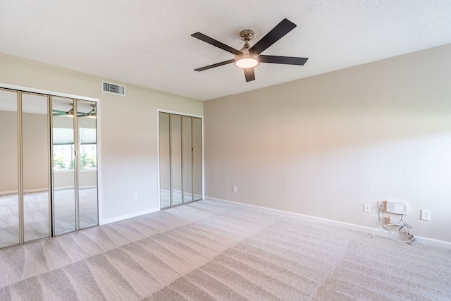 unfurnished bedroom with light carpet, a textured ceiling, ceiling fan, and multiple closets