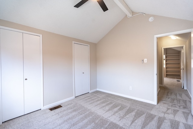 unfurnished bedroom with multiple closets, ceiling fan, lofted ceiling with beams, and light carpet