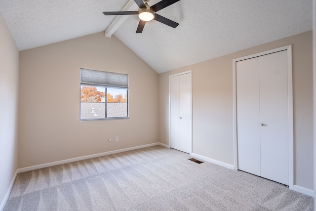 unfurnished bedroom featuring multiple closets, ceiling fan, light carpet, and vaulted ceiling with beams