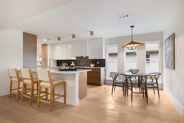 kitchen with white cabinets, custom range hood, light wood-type flooring, and an island with sink