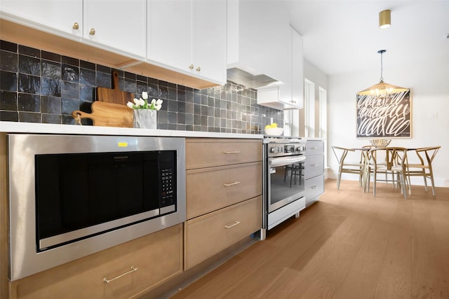 kitchen featuring decorative backsplash, appliances with stainless steel finishes, decorative light fixtures, light hardwood / wood-style floors, and white cabinetry