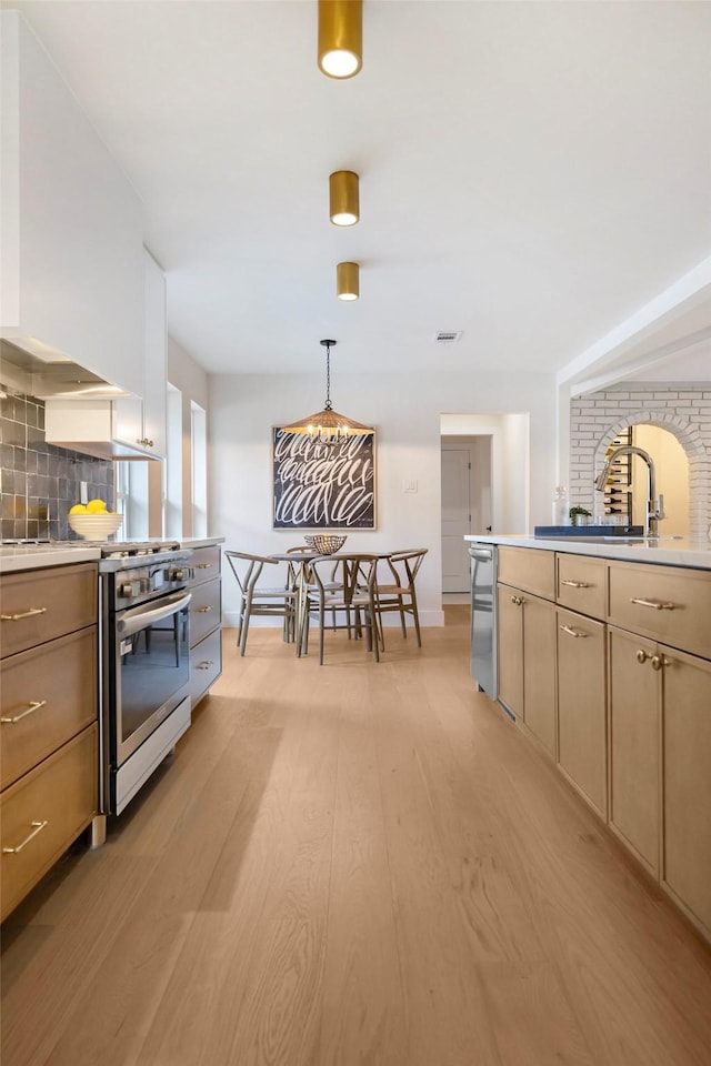 kitchen featuring light brown cabinetry, tasteful backsplash, high end stainless steel range oven, light hardwood / wood-style flooring, and hanging light fixtures