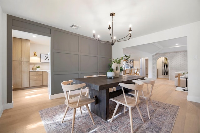 dining area featuring a chandelier, lofted ceiling, light hardwood / wood-style floors, and brick wall