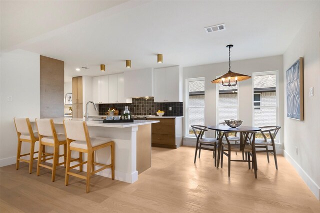 kitchen with white cabinetry, a center island with sink, custom range hood, and light wood-type flooring