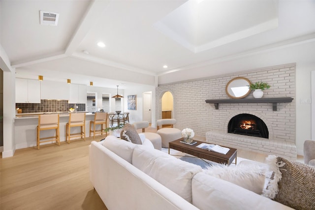 living room featuring a fireplace, beam ceiling, and light hardwood / wood-style flooring