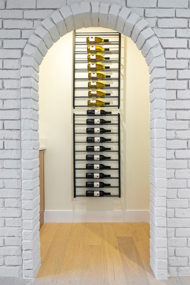 wine area featuring wood-type flooring and brick wall