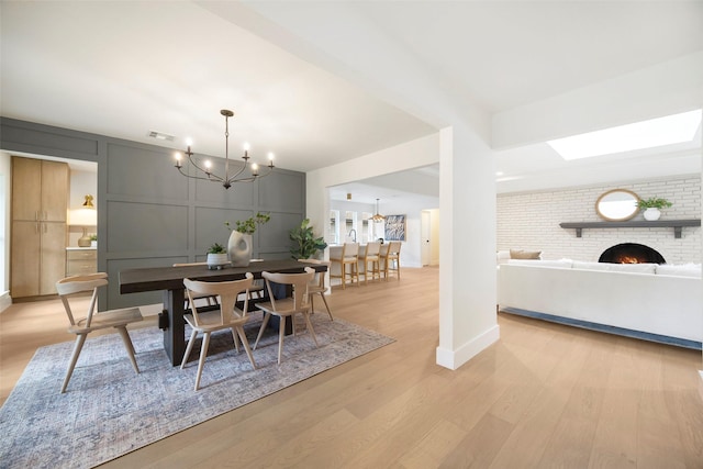 dining space with light hardwood / wood-style floors, a notable chandelier, and a brick fireplace