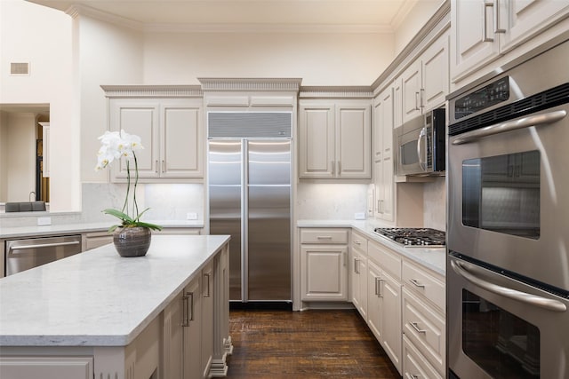 kitchen with light stone counters, dark hardwood / wood-style flooring, backsplash, crown molding, and appliances with stainless steel finishes