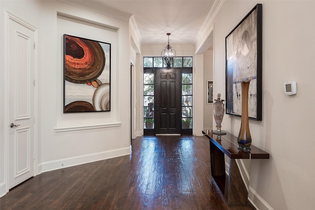 entrance foyer featuring dark wood-type flooring, ornamental molding, and an inviting chandelier