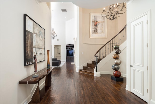 entryway with a towering ceiling, dark hardwood / wood-style floors, crown molding, and a notable chandelier