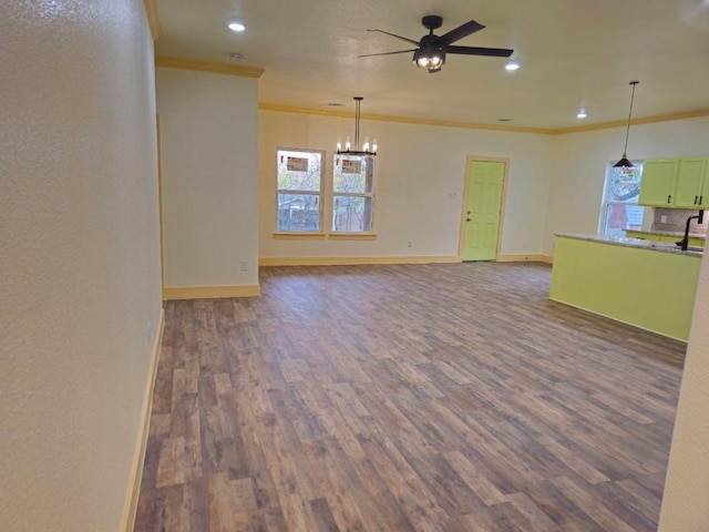 unfurnished living room with crown molding, sink, ceiling fan with notable chandelier, and dark wood-type flooring