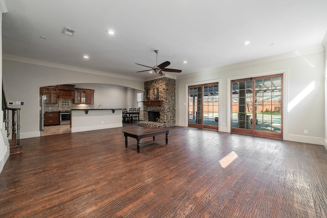 living room with dark hardwood / wood-style flooring, a stone fireplace, ceiling fan, and crown molding